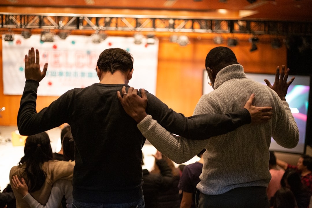 Two men with arms around each other's shoulders raise hands in unity.